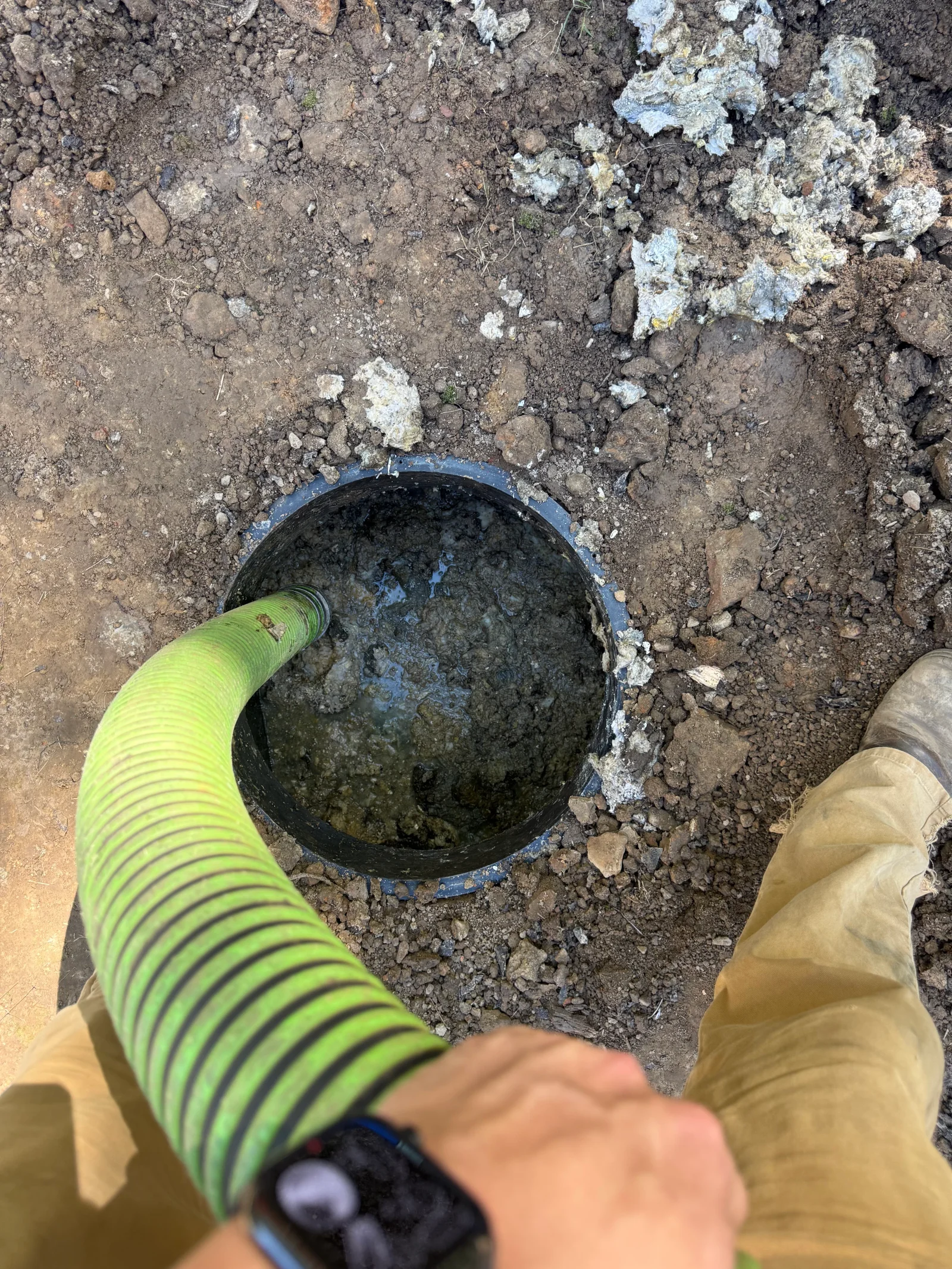 Septic tank opening with green vacuum hose connected for inspection and cleaning service