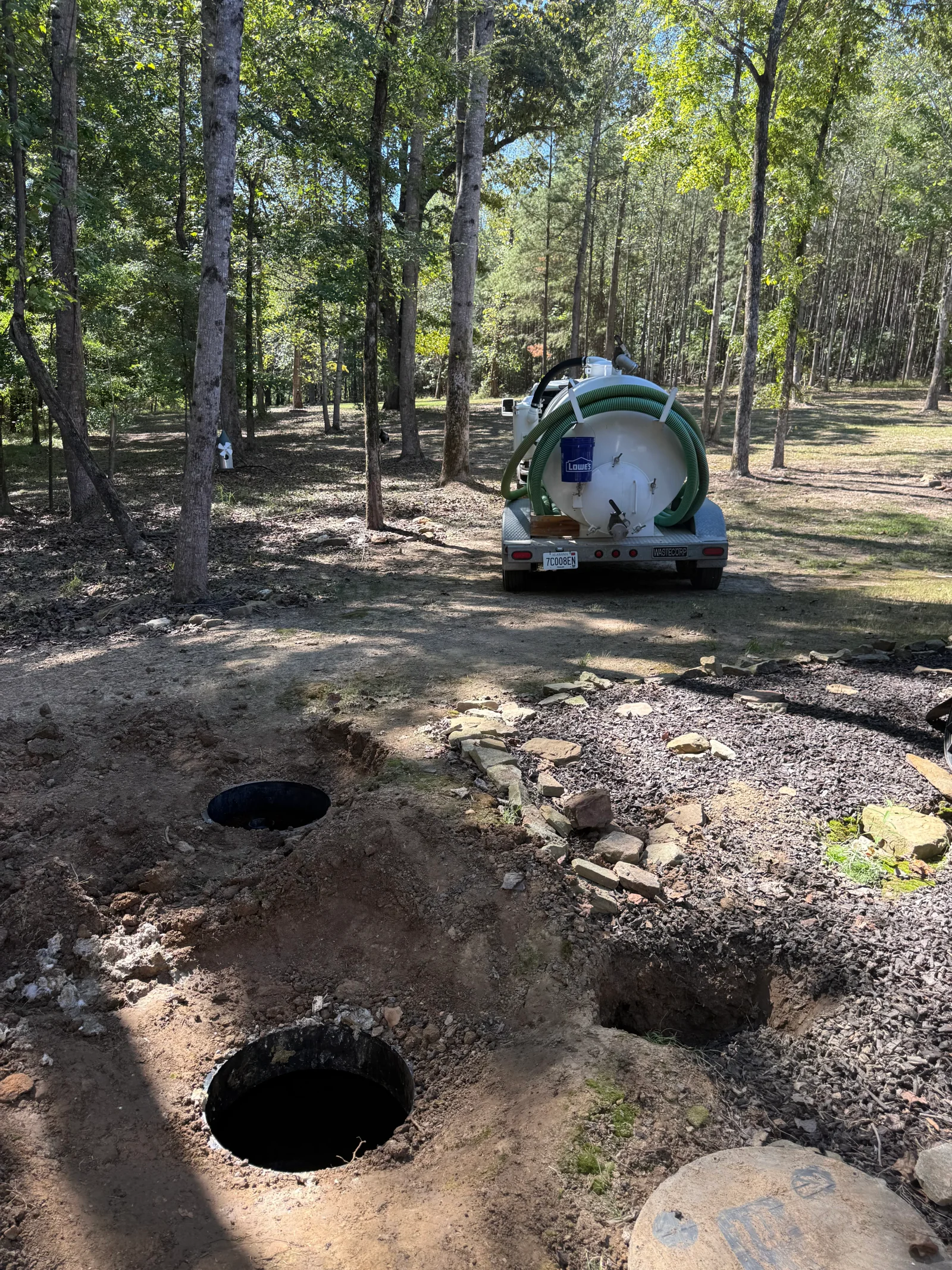 Septic pumping truck with large tank servicing multiple septic access points in wooded area