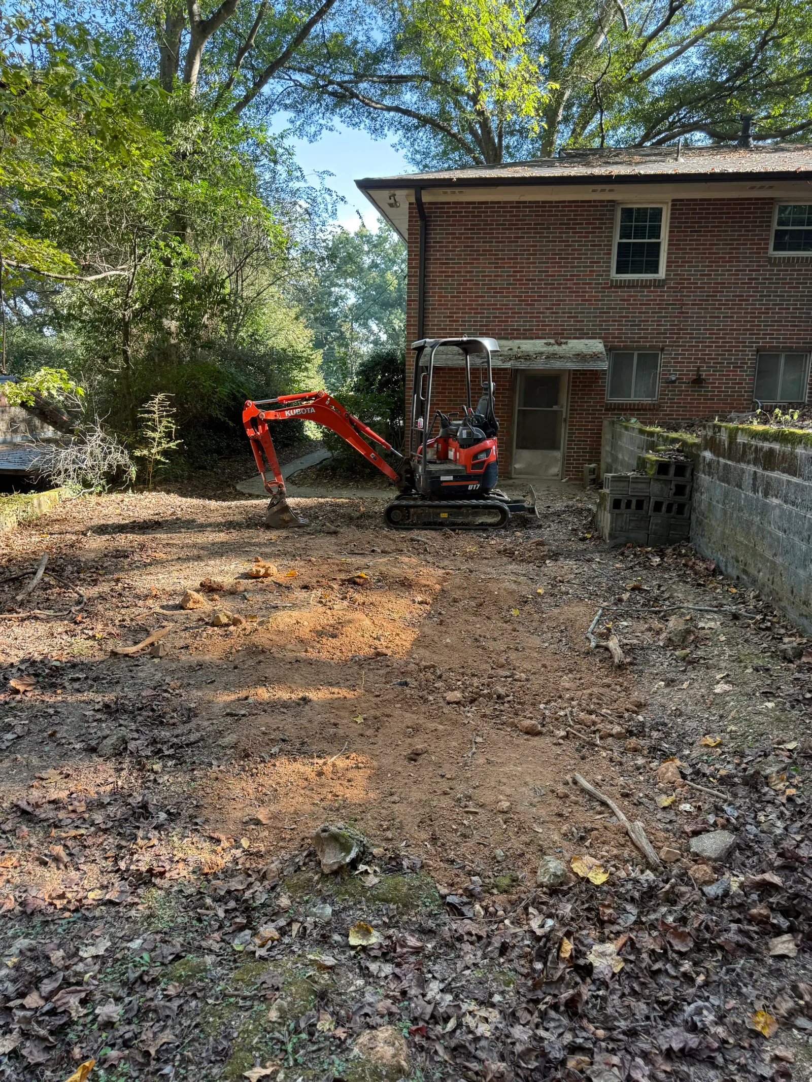 Red mini excavator clearing debris and vegetation from residential septic work area