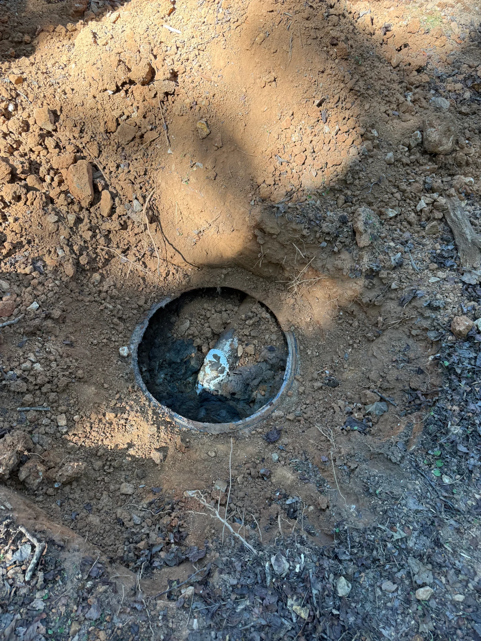 Exposed septic tank opening in excavated soil showing tank interior with deposits