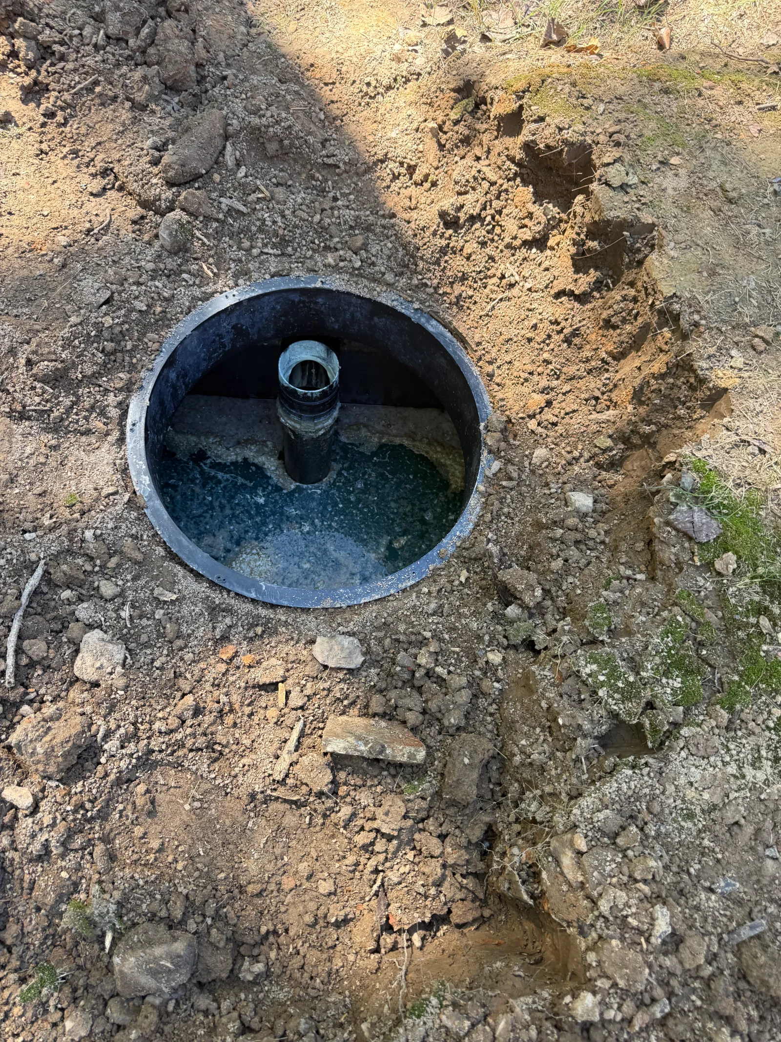 Installed septic tank with concrete riser and access lid in excavated soil pit